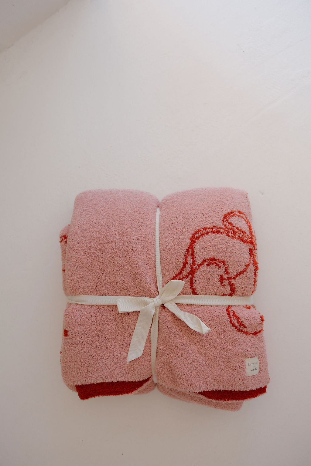 The Minty Cherries Plush Blanket | Iconic Cherry, an Oeko-Tex certified pink microfiber blanket with red cherry designs and a white ribbon, adds softness and style to your space.