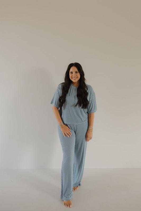 A woman with long dark hair wears the forever french baby Women's Boxy Tee Lounge Set in Blue Gingham, standing barefoot against a plain light background and smiling at the camera.
