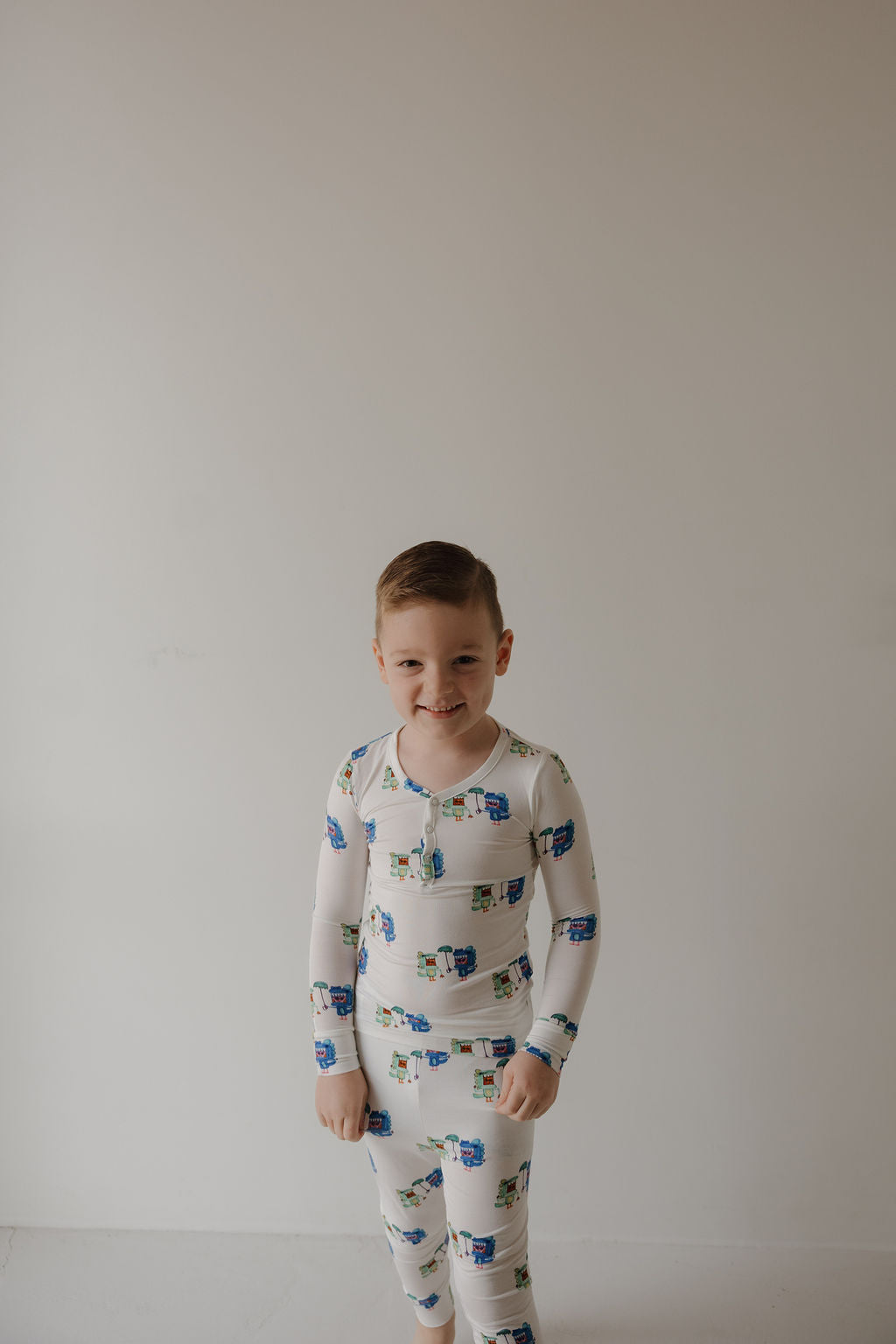 A young child smiles in forever french baby's Bamboo Two Piece Pajamas | Charli's Monsters, featuring colorful monster patterns and hypoallergenic fabric, against a plain white background.