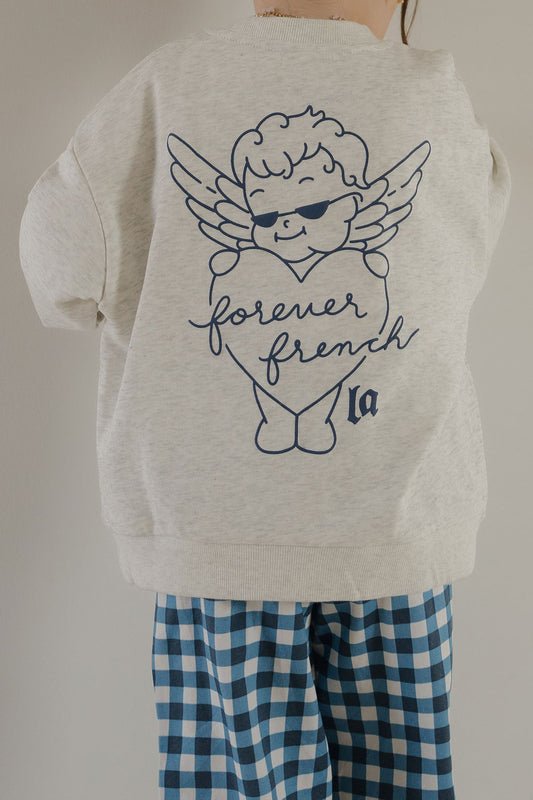 A child wears the forever french baby Child Sweatshirt | ff Los Angeles, featuring a winged cherub in sunglasses holding a "forever french" heart—perfect for matching family outfits.