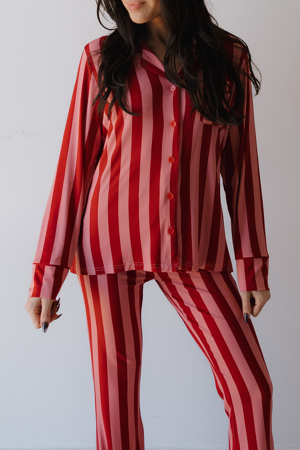 A woman models the Minty Cherries Women's Bamboo Button Up Lounge Set in Iconic Stripe—featuring bold red and pink stripes—against a plain white background.