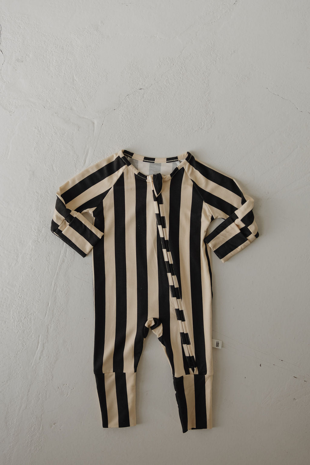 The Bamboo Zip Pajamas in Midnight Stripe by forever french baby, featuring black and beige vertical stripes, are hypoallergenic, long-sleeved, and breathable—perfect baby sleepwear laid flat on a light textured surface.