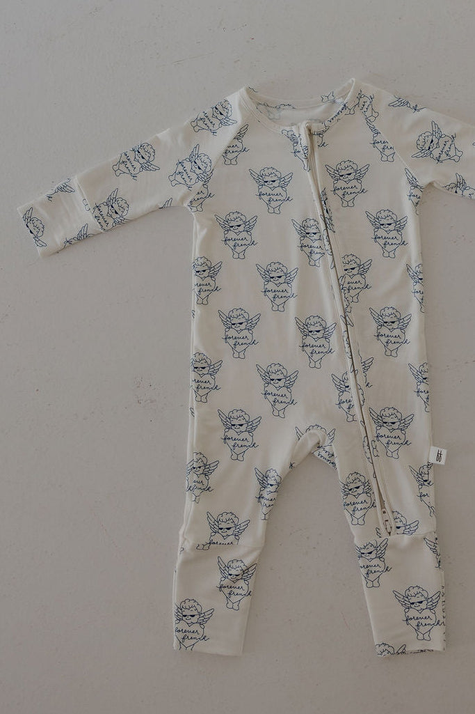 The Bamboo Zip Pajamas by forever french baby are cream-colored bamboo onesies with long sleeves, a blue cherub print, and a diagonal neck-to-leg zipper—hypoallergenic sleepwear for your little one’s comfort.