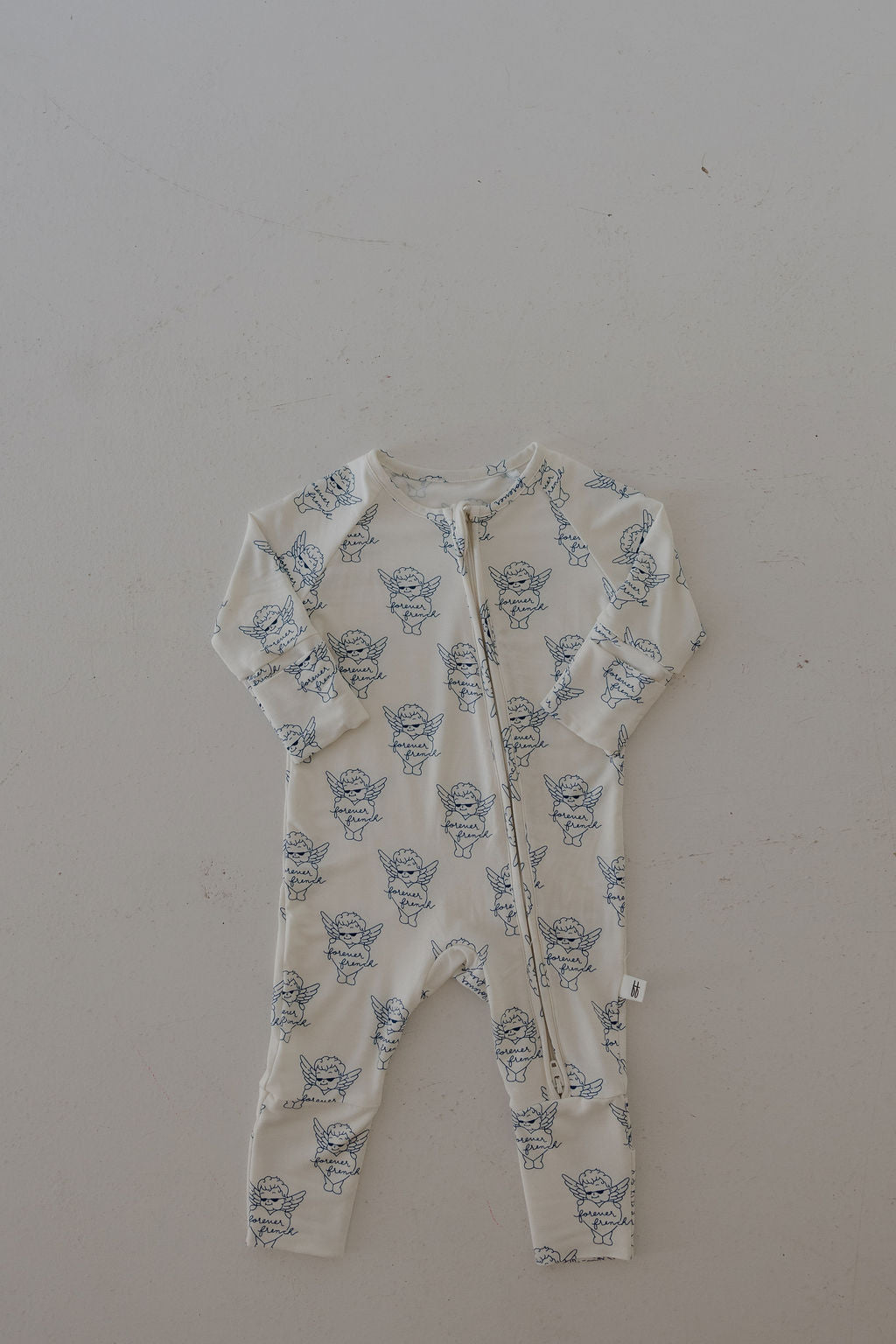 The Bamboo Zip Pajamas by forever french baby are cream-colored bamboo sleepwear for babies, featuring blue cartoon animal prints and a diagonal front zipper, displayed flat on a light background.