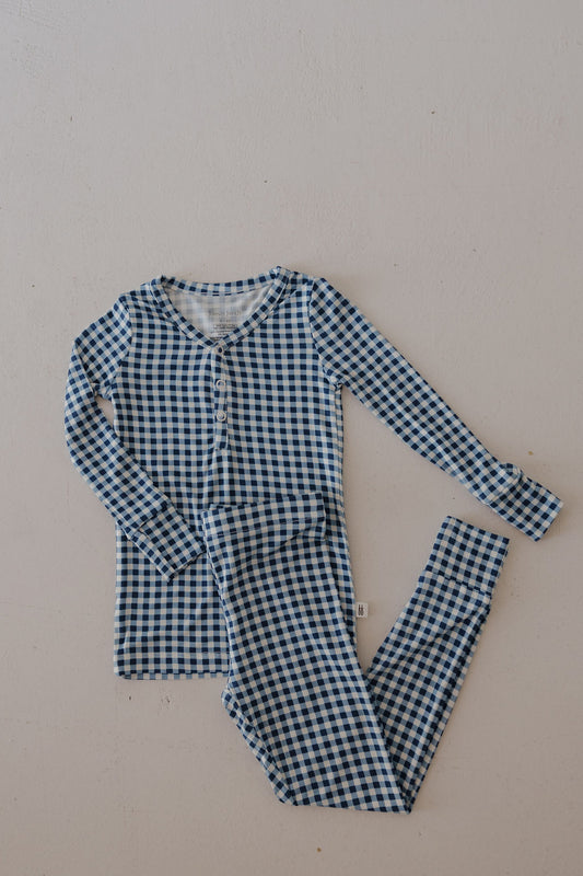 The forever french baby Bamboo Two Piece Pajamas in Blue Gingham are hypoallergenic kids' sleepwear, featuring a breathable long-sleeve button-up top and matching pants, shown laid flat on a light background.