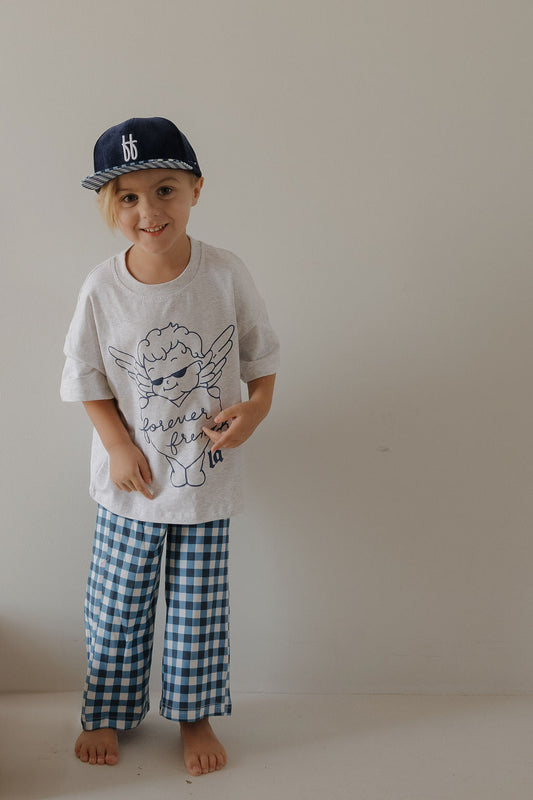 A young child wears the forever french baby T-Shirt & Pant Set | ff Los Angeles—a playful, angel-graphic white tee and blue gingham pants—perfect for expressing LA-inspired kids style.