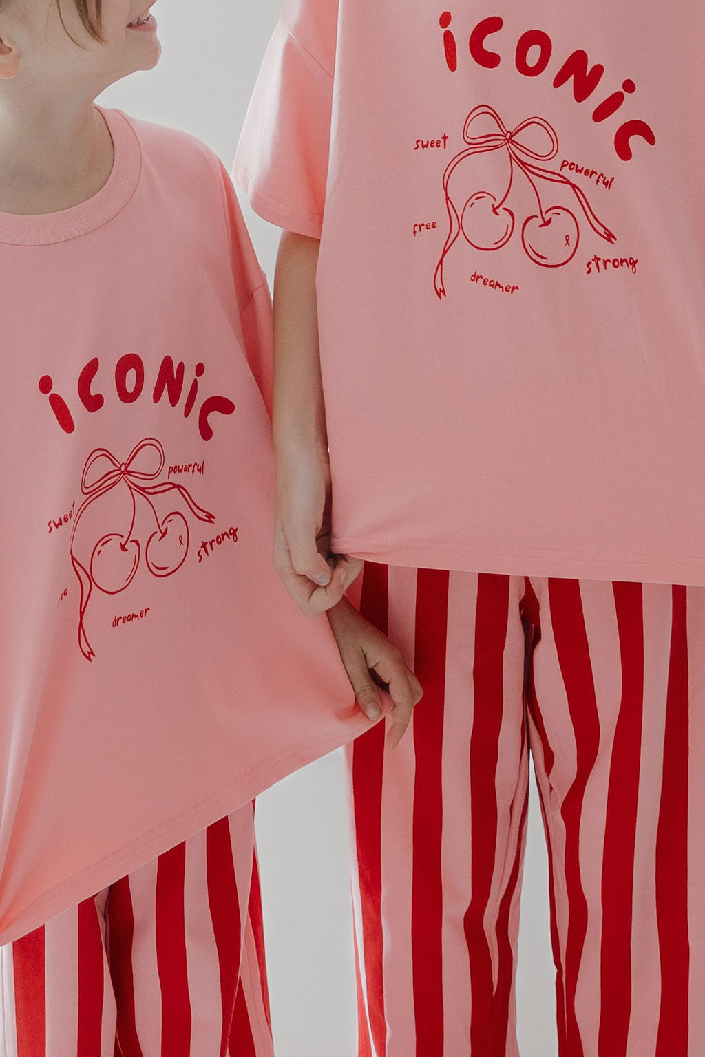 Two kids shine in the Minty Cherries T-Shirt & Pant Set | Iconic Cherry & Stripe: oversized pink tees with hand-drawn cherry graphics and uplifting text, matched with bold red-and-white striped pants—perfect for young dreamers and trendsetters.