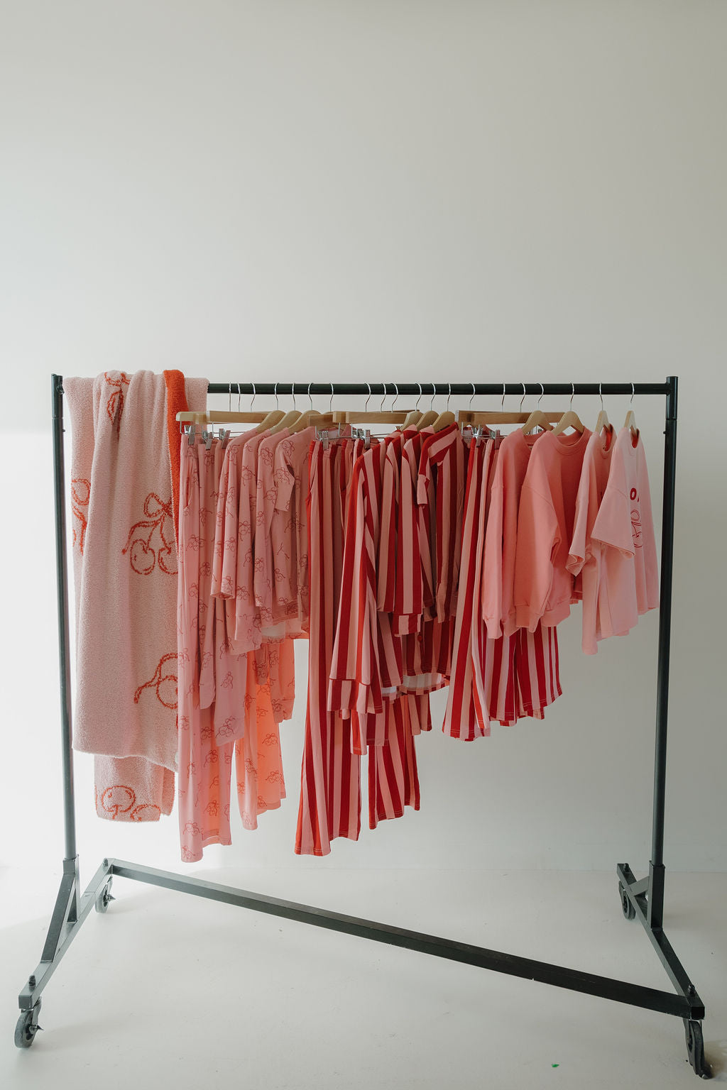 A wooden rack displays Minty Cherries' Women's Boxy Tee Lounge Set in Iconic Cherry, featuring pink and red tones with patterned bamboo fabric, neatly hung on wooden hangers against a white background.