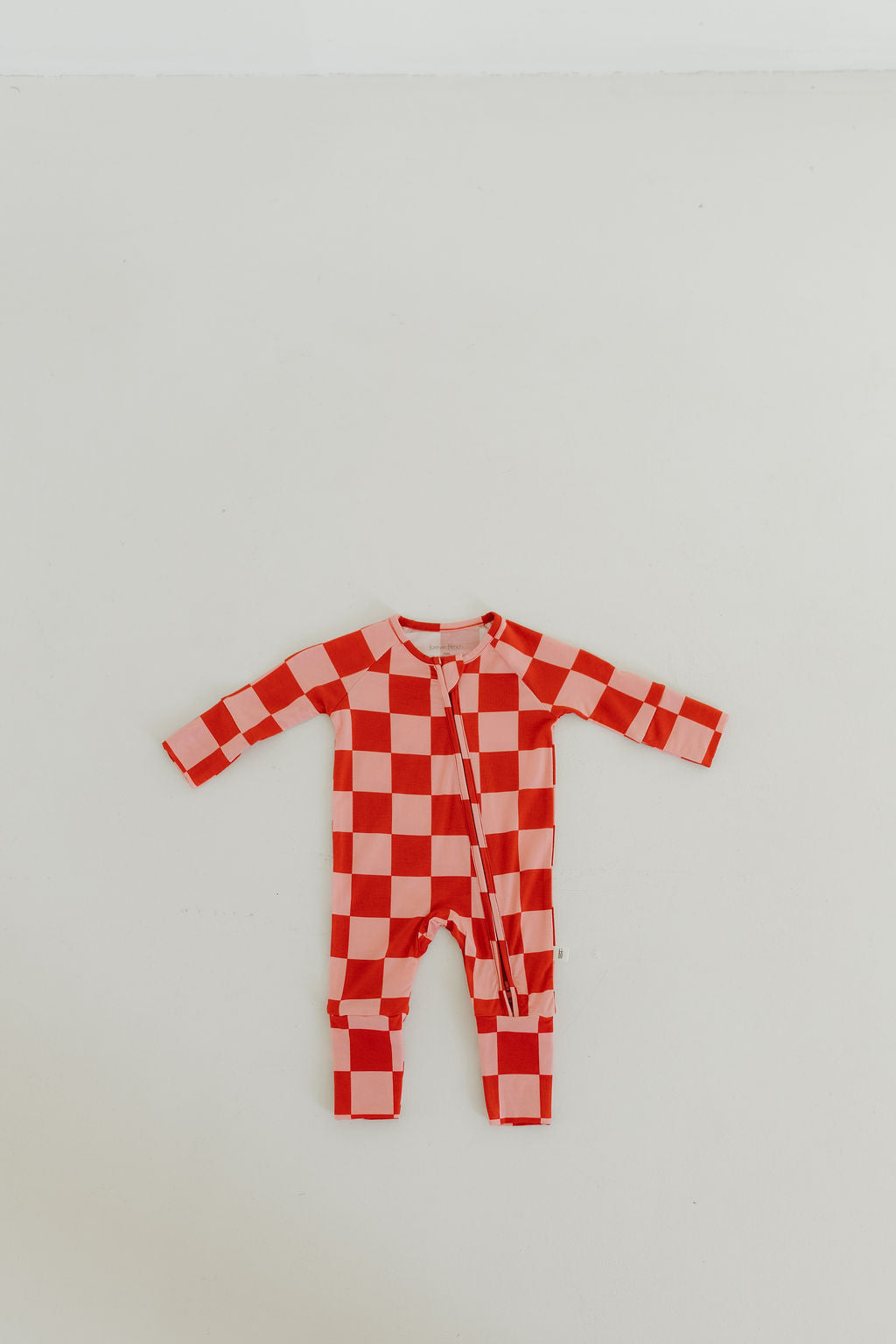 The Bamboo Zip Pajamas | XOXO by forever french baby, featuring a red and white checkered design with long sleeves, made from breathable materials, is laid flat on a beige background.