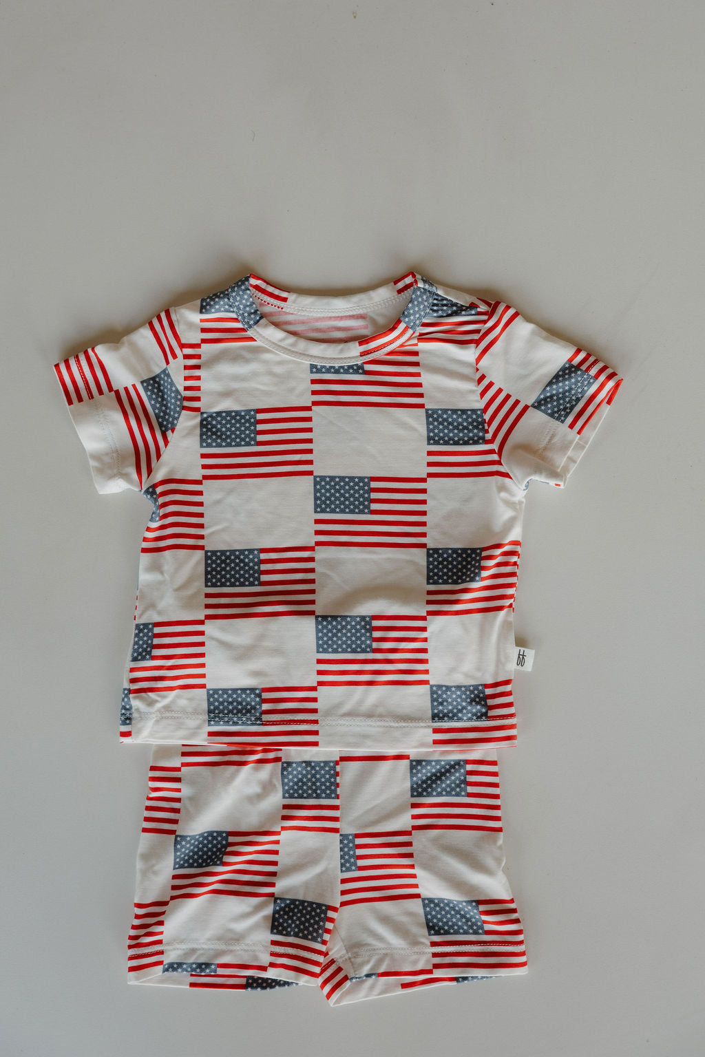 The forever french baby Bamboo Short Set | Americana features a breathable bamboo shirt and shorts with American flags and red, white, and blue stripes, shown laid flat on a light gray surface.