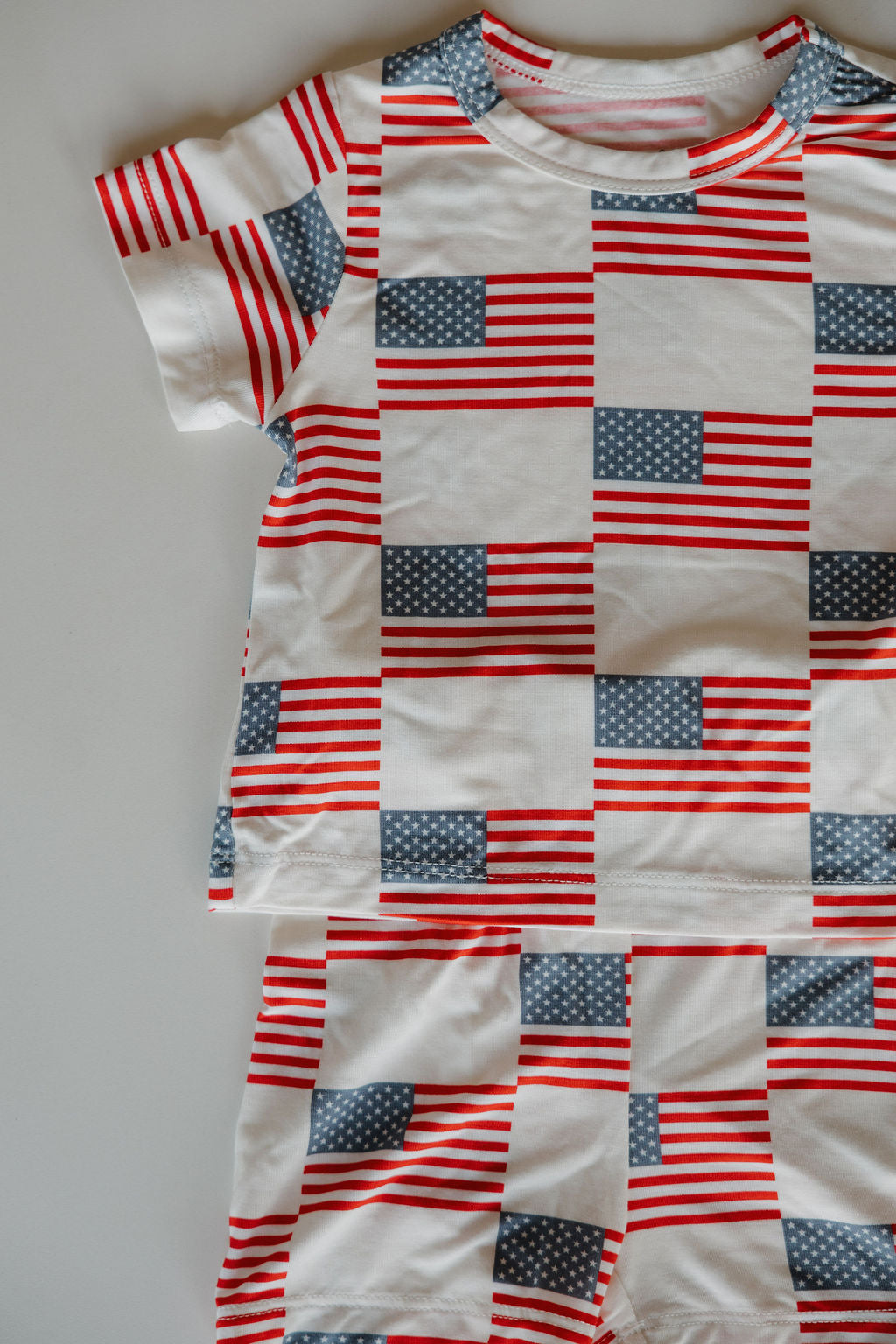 The Bamboo Short Set | Americana by forever french baby features a repeating American flag pattern in red, white, and blue on white, made from breathable bamboo fabric and shown laid flat on a light surface.