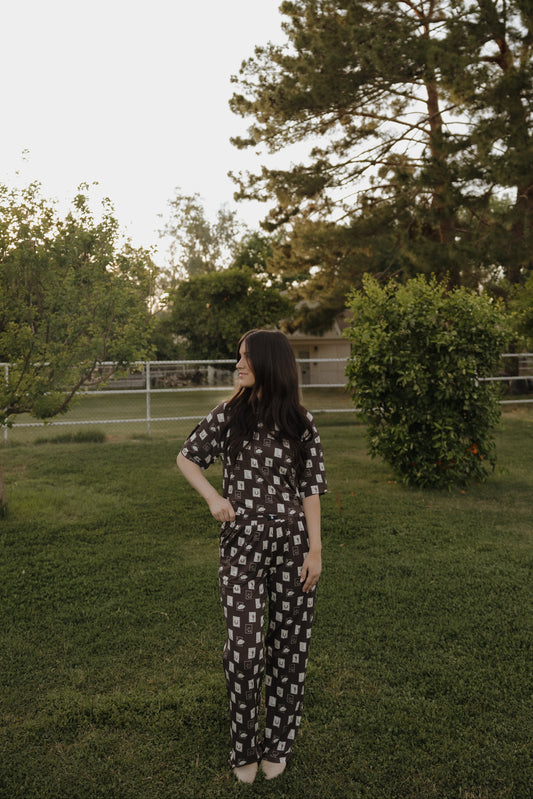 A woman with long, dark hair stands on a grassy lawn wearing the Women's Boxy Tee Lounge Set by forever french baby from With Love from AZ. She looks to her left, with trees and a fence in the background.
