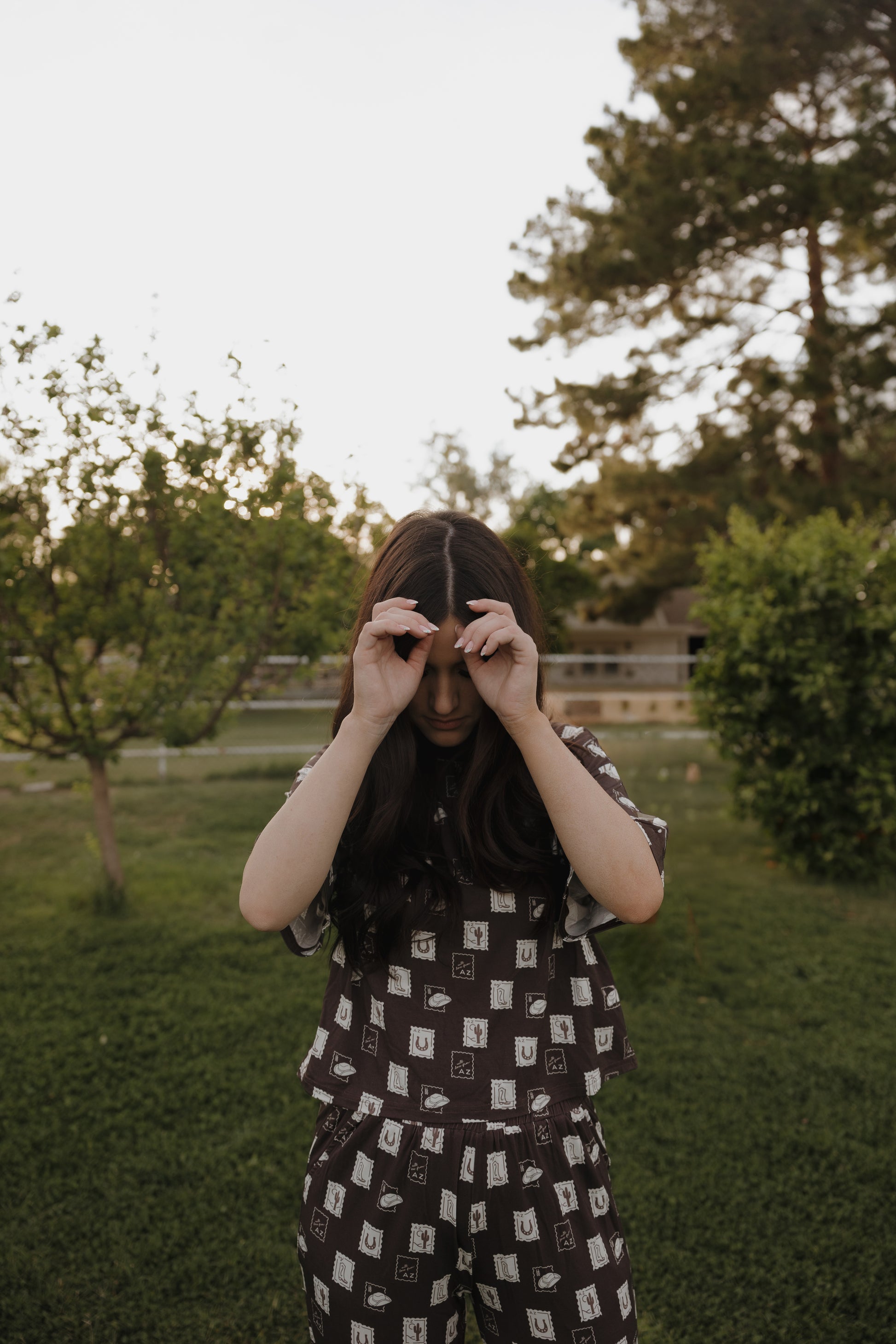 A person with long dark hair stands on grass in the forever french baby Women's Boxy Tee Lounge Set | With Love from AZ, holding their hands near their eyes as if making binoculars, with trees and greenery in the background.