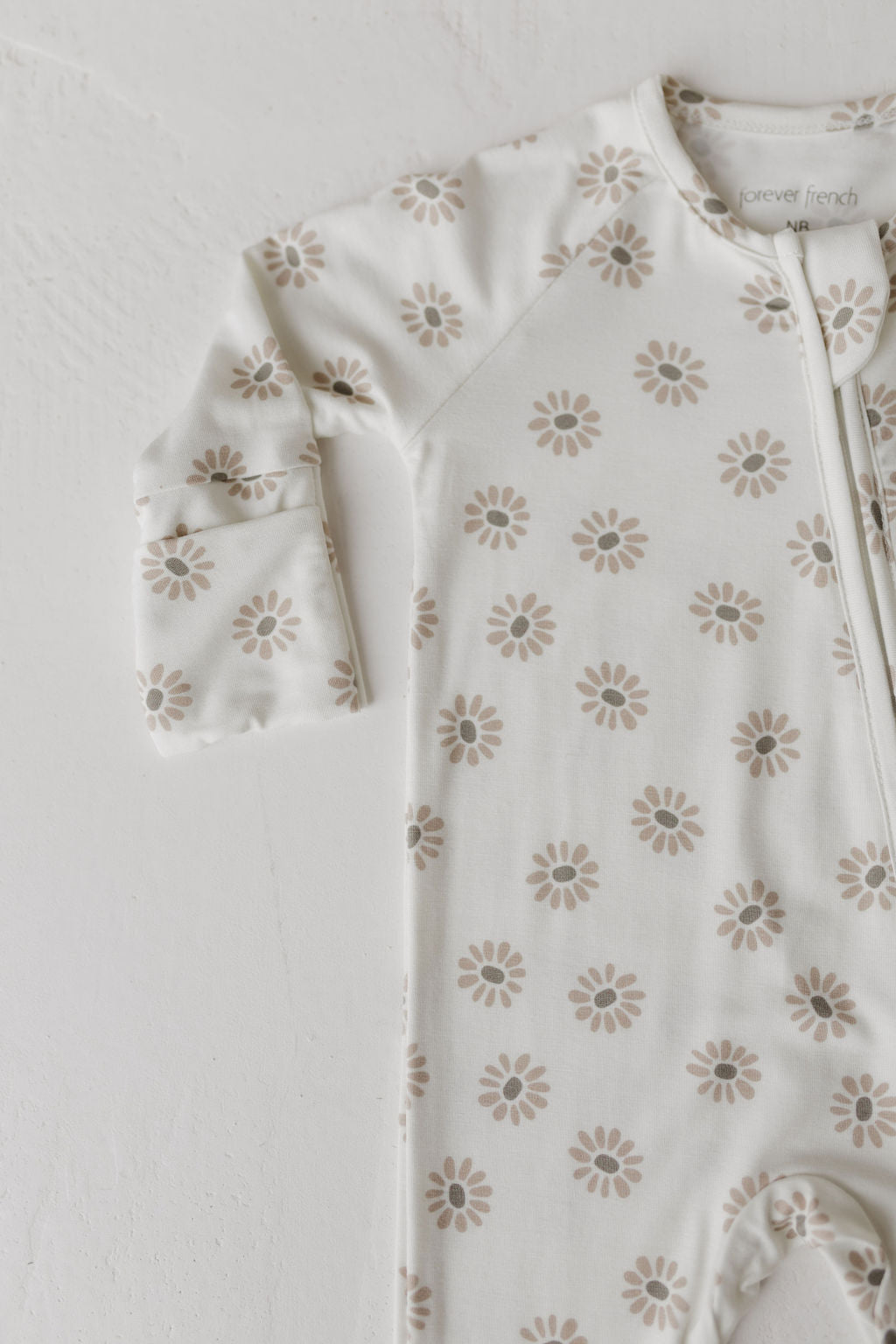 The Bamboo Zip Pajamas from forever french baby, in the Daisy Fields pattern, are beige with long sleeves and a light brown floral design, shown on a white surface.