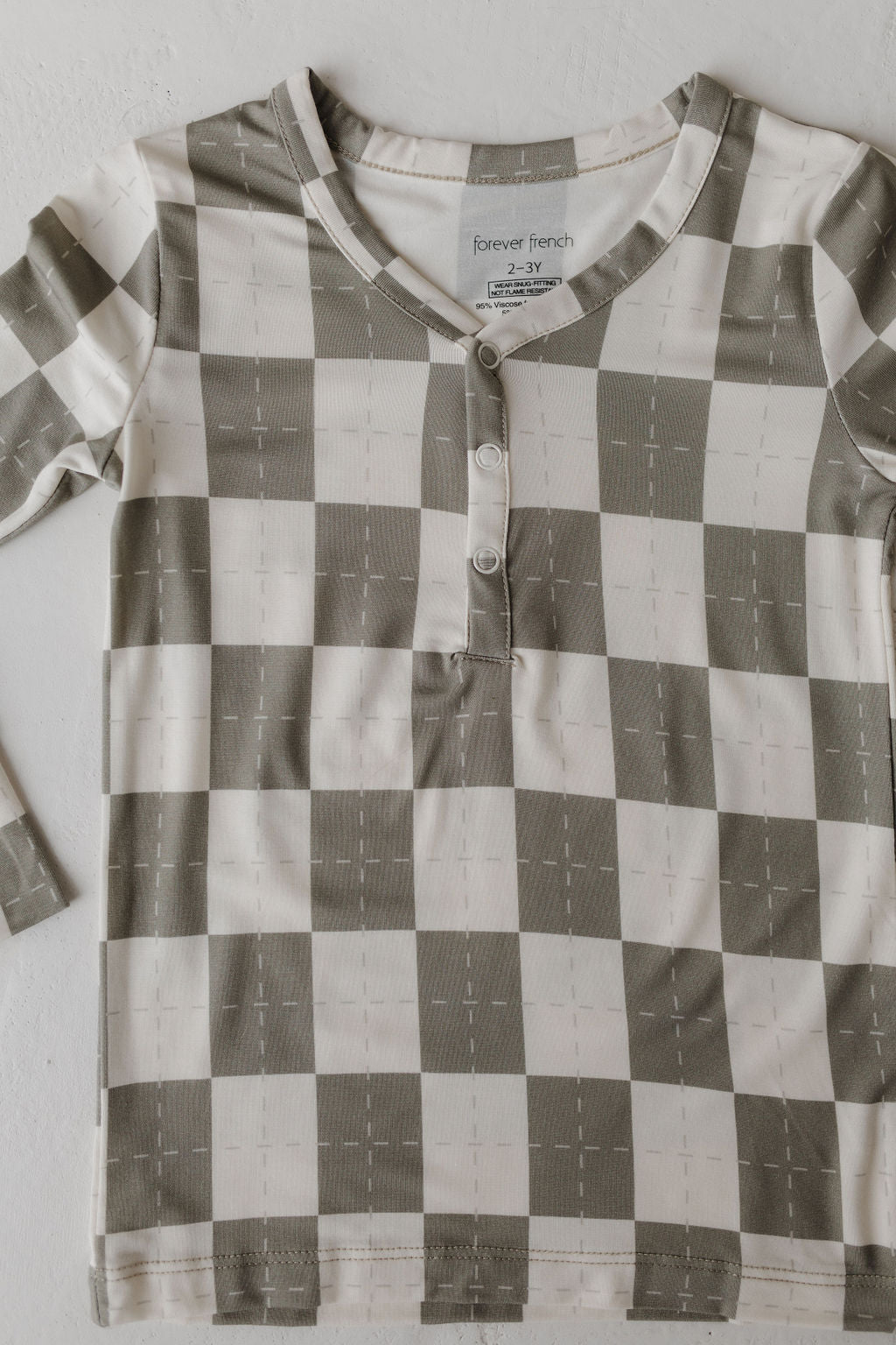 A long-sleeved, button-up shirt with a green and white checkered pattern is crafted from breathable fabric. The label reads "forever french baby 2 - 3 Y." Laid flat on a plain background, it promises comfort for little ones.