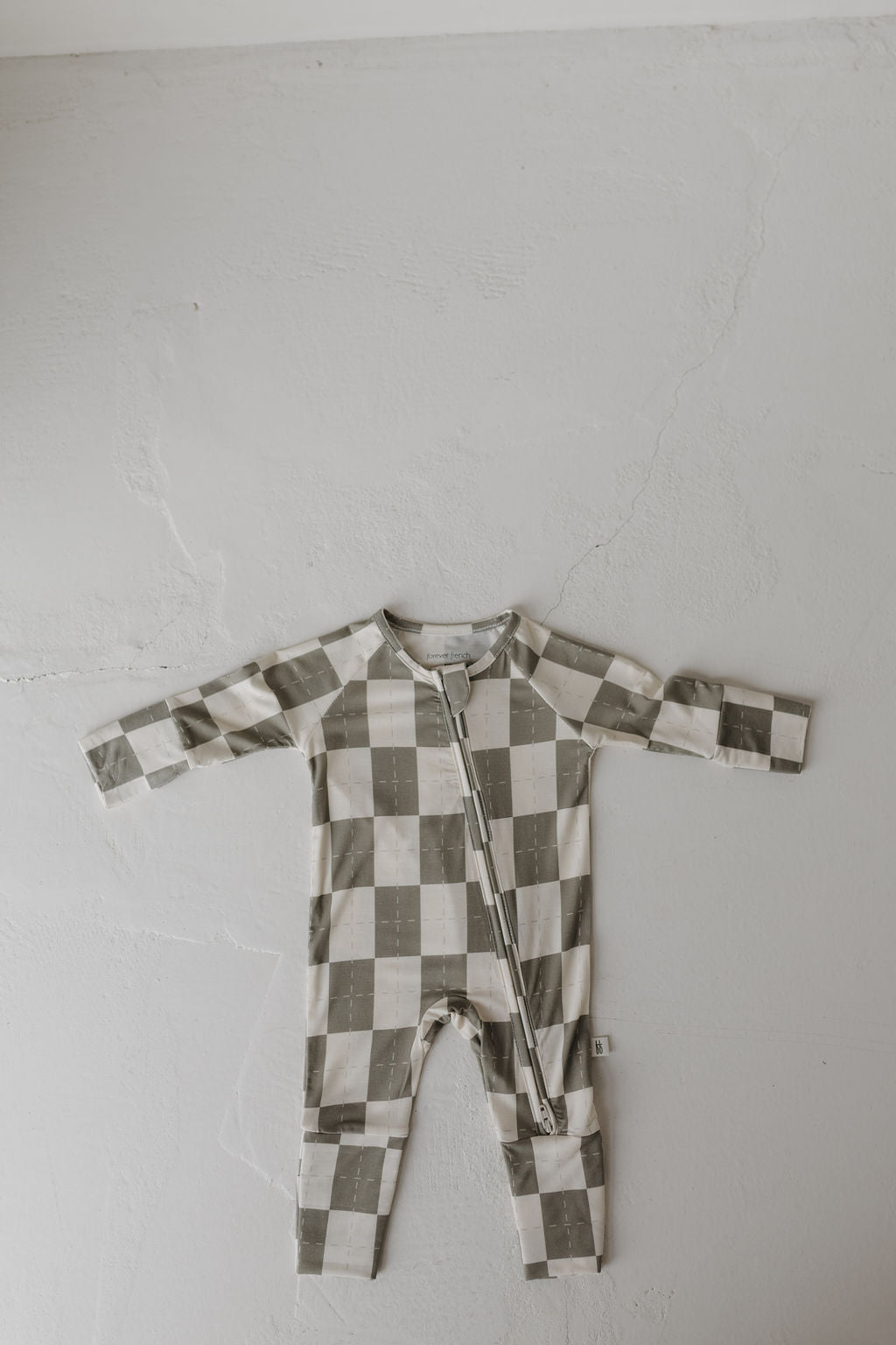 The Bamboo Zip Pajamas | Oat & Sage from forever french baby lay flat on a light, textured surface. Made of breathable bamboo, these pajamas highlight a green and white checkered pattern with a stylish zipper front for ultimate comfort.