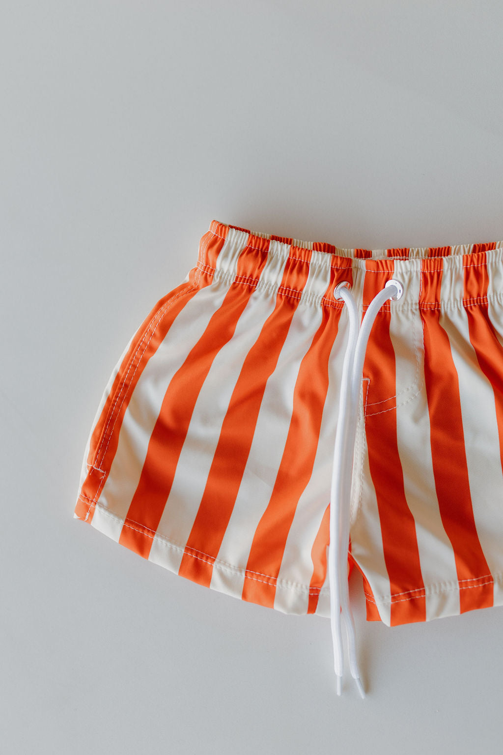 Part of the Poolside Collection by forever french baby, the Child Boardshorts feature orange and white stripes with a white drawstring, beautifully set against a light background.