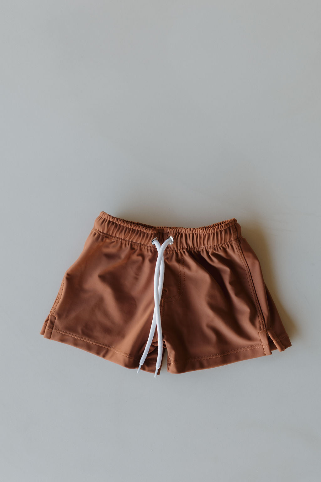 From the Terra collection by forever french baby, the Child Boardshorts feature white drawstrings and an elastic waistband for a customizable fit. Laid flat on a light gray surface, this simple brown design is ideal for casual wear or swimming.