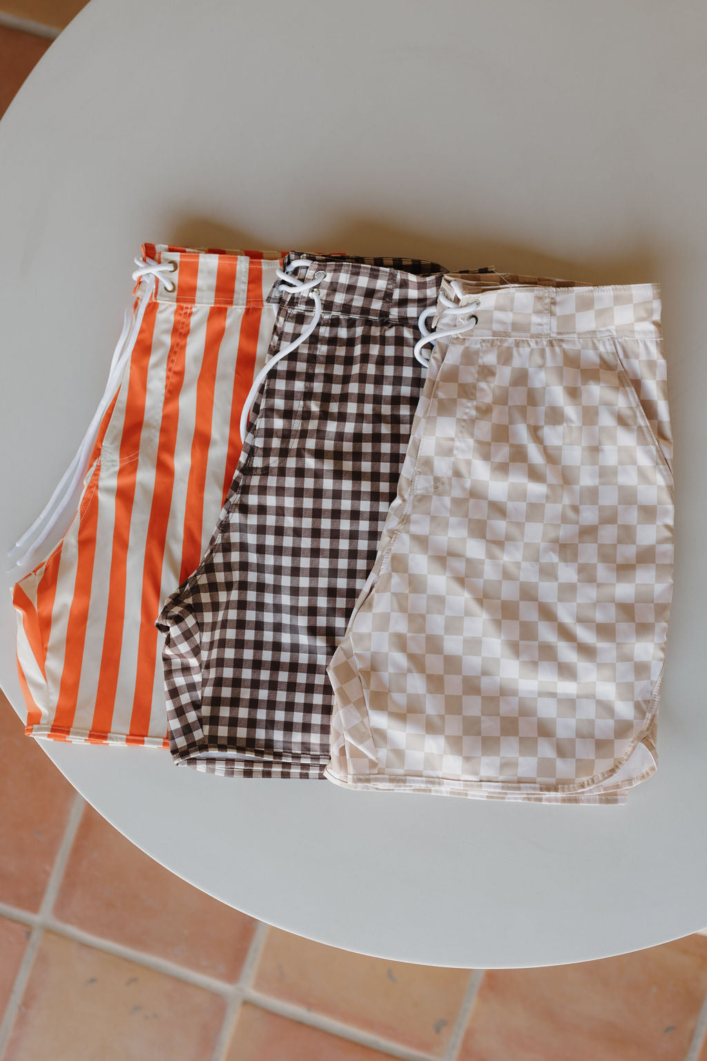 From the Poolside Collection by forever french baby, the Men's Boardshort offers three styles: vibrant orange and white stripes, classic brown and white checks, and chic beige and white checks—ideal for sun-drenched water's edge outings.