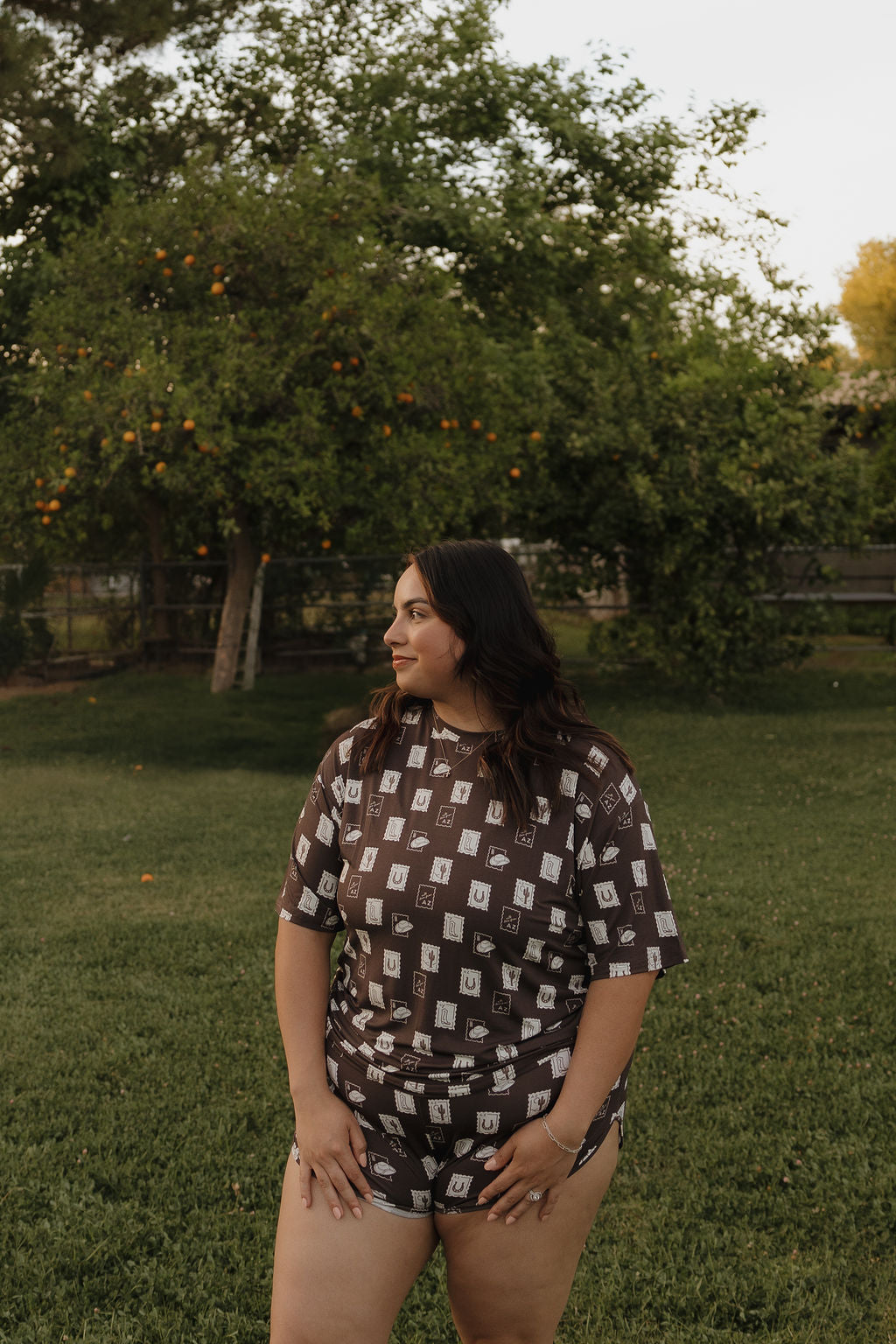 A woman stands on grass in front of trees, wearing the forever french baby Women's Bamboo Short Set | With Love from AZ. She looks to the side, hands on her thighs, enjoying the outdoors in this stylish and breathable set surrounded by greenery.