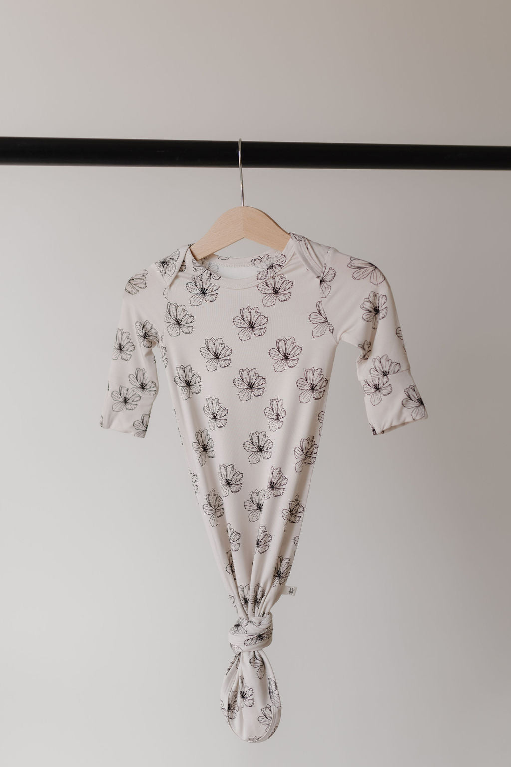 The Bamboo Knotted Gown in Desert Bloom by forever french baby features a black floral pattern on a white background, hanging gracefully knot-tied at the bottom. Made from hypo-allergenic bamboo, it offers the gentle embrace perfect for newborns.