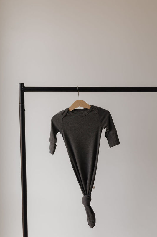 A Bamboo Knotted Gown in Shadow by forever french baby, hypo-allergenic and long-sleeved, hangs elegantly from a wooden hanger on a minimalist black metal rack against a light beige backdrop.