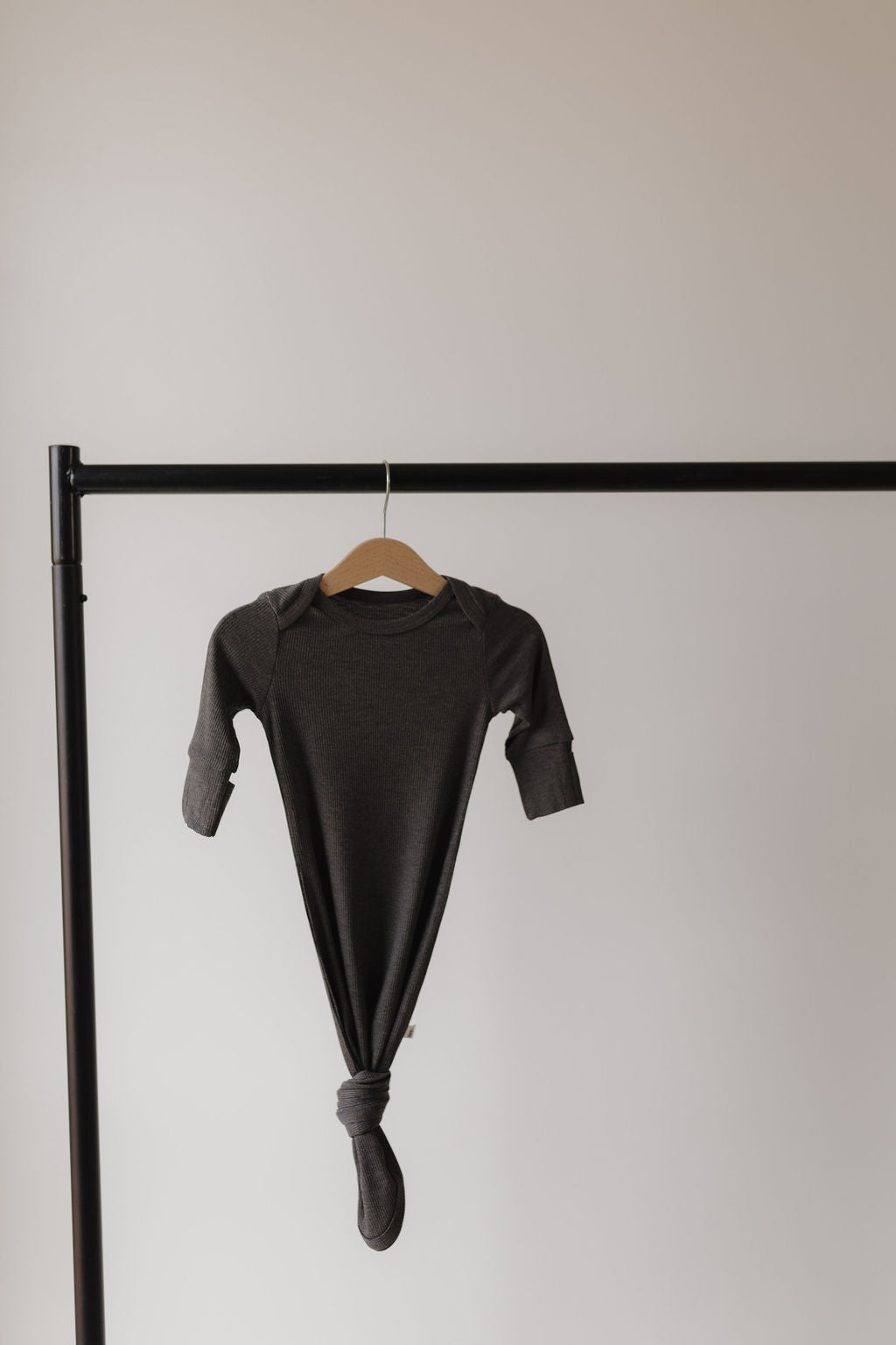 The Bamboo Knotted Gown | Shadow by forever french baby, crafted from hypo-allergenic bamboo clothing, is knotted at the bottom and hangs on a wooden hanger from a black metal rack against a plain light gray background.