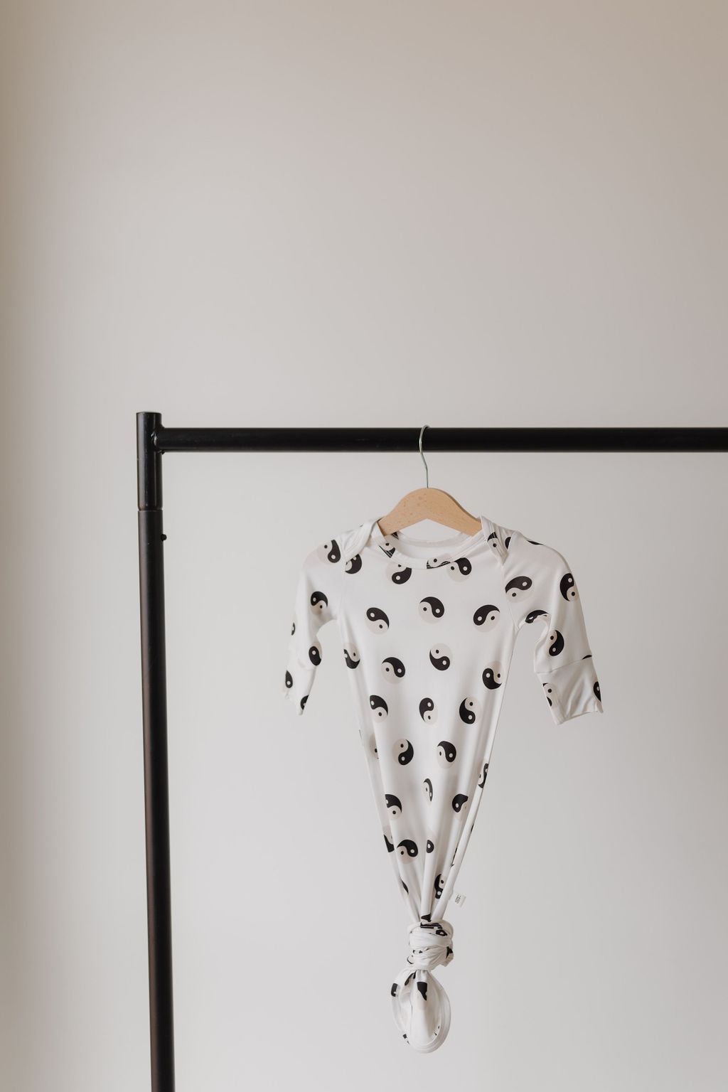 The Bamboo Knotted Gown by forever french baby features a black and white yin-yang pattern, hanging on a wooden hanger. Displayed on a black metal rack against a light background, it embodies the essence of hypoallergenic clothing for your newborn.