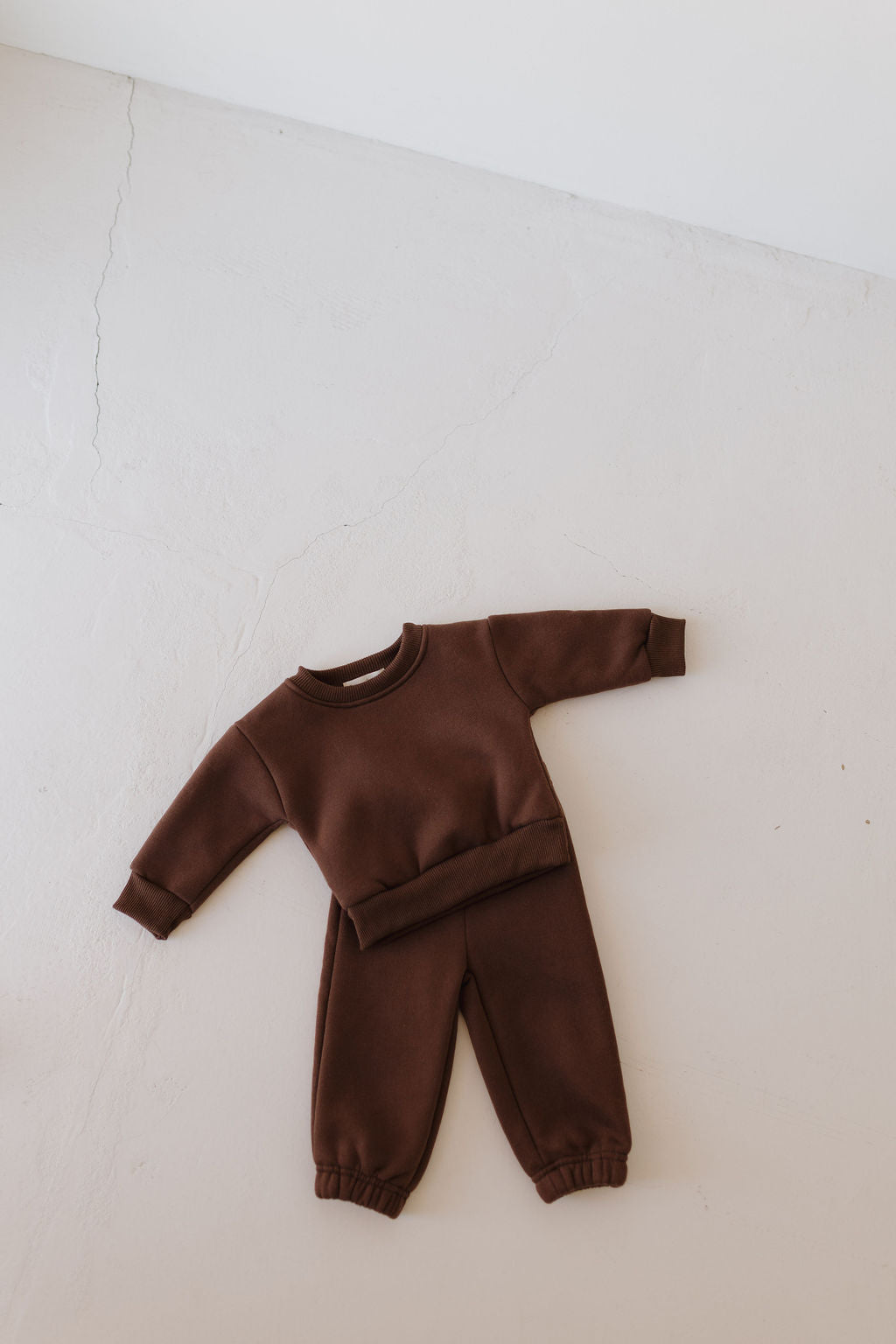 Displayed on a pale surface, the Sweat Set | Driftwood by forever french baby features a brown toddler sweatshirt and jogger pants with long sleeves and cuffed pants. An elastic waistband provides all-day comfort, enhancing its cozy look.