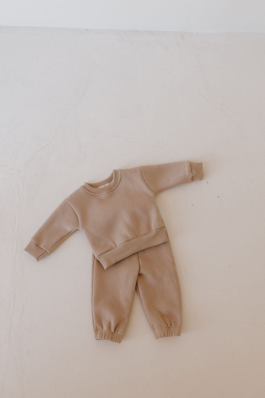 The "Sweat Set | Fawn" by forever french baby features a beige toddler's sweatshirt and sweatpants laid flat on a light surface. The set, with an elastic waistband and super soft fabric, is perfect for cozy wear with arms and legs slightly extended.