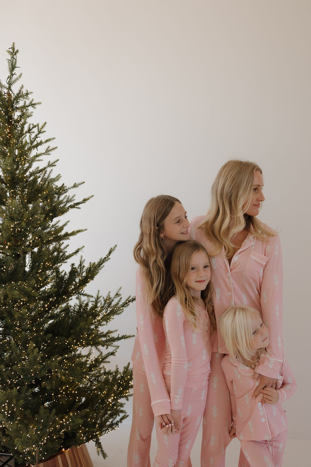 Four people, possibly a mom and three daughters, smile together by a Christmas tree in matching forever french baby Long Sleeve Toddler Bamboo Pajamas | Nutcracker.