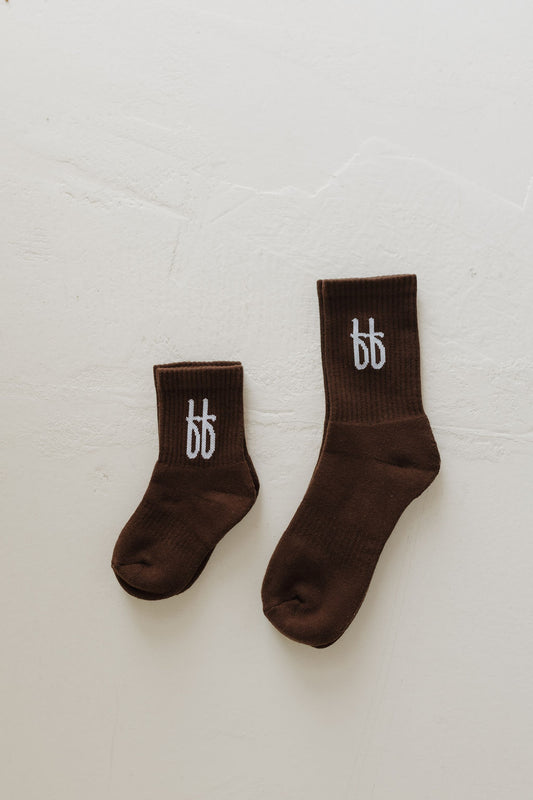 A pair of ff Crew Socks in Cocoa from forever french baby lies on a light surface—one larger for adults and one smaller for children. Each features a stylish white "bb" logo at the top.