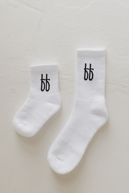 A comfy pair of white ff Crew Socks, by forever french baby, each featuring the black "bb" logo on the ankle and one slightly smaller than the other, displayed on a light textured surface—ideal for everyday wear.