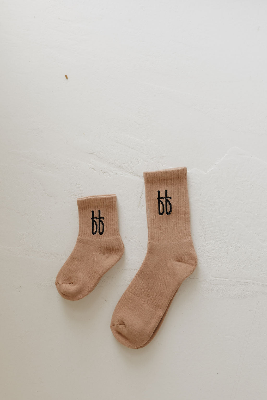 Two ff Crew Socks | Sandstone from forever french baby, one larger and one smaller, are laid flat on a light surface with a black double "b" logo near the top. Positioned with toes pointing upward, these socks make an ideal everyday choice.