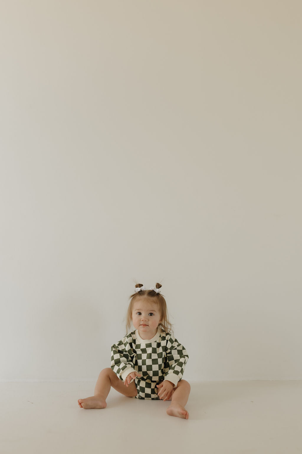 A toddler with pigtails sits on the floor against a plain white background, wearing the charming "Lucky" sweatshirt romper in black and white checkered cotton elastane by forever french baby.