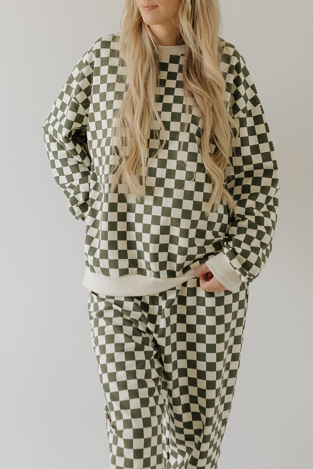 A person wears the forever french baby Adult Sweat Set | Lucky in green and white checkered pattern, ideal for cooler weather, complemented by long wavy blonde hair against a plain light-colored background.