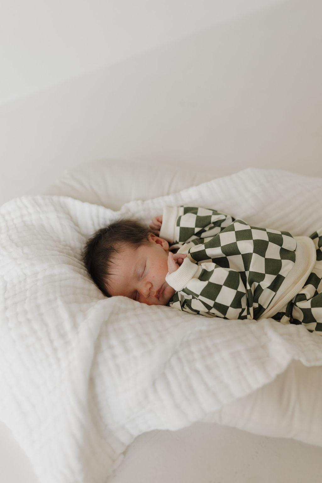 A sleeping baby lies comfortably on a soft, white blanket, dressed in the "Lucky" Sweat Set by forever french baby. The tranquil scene is enhanced by cooler weather and a neutral background.