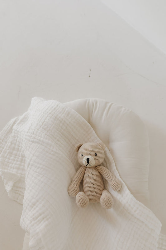 Benson the Bear, a beige knit doll from forever french baby, rests on a white pillow with a textured blanket. The serene white surface enhances its cozy charm, making it an ideal accessory.