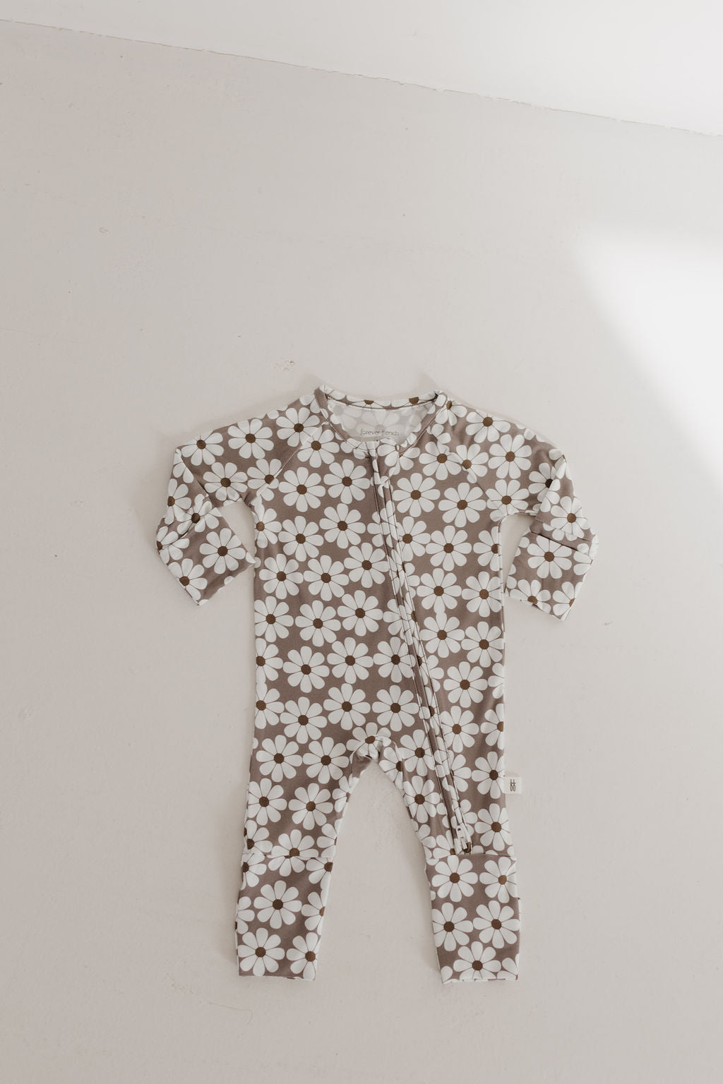 The Bamboo Zip Pajamas | Darlin' by forever french baby is a long-sleeve onesie with white flowers on a brown background, made from breathable fabric, displayed against a plain light-colored wall.