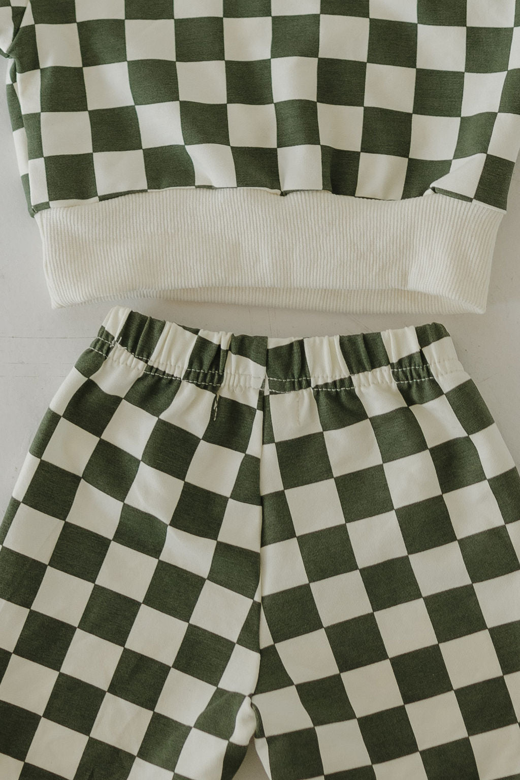 The "Lucky" sweat set by forever french baby, featuring a green and white checkered pattern, is displayed on a white surface. This charming adult matching set includes a long-sleeve top with ribbed hem and elastic waist pants, both showcasing the bold design.