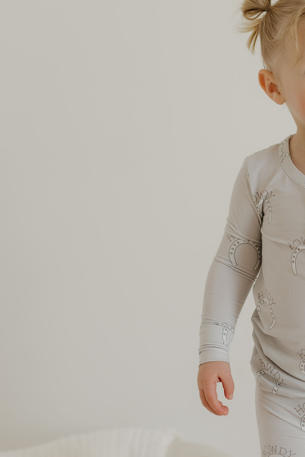 A toddler partially visible, with light hair in pigtails, wears the Bamboo Two Piece Pajamas in light gray from forever french baby. The outfit features breathable, hypoallergenic fabric with subtle patterns and stands against a plain background, showing only part of the face and upper body.