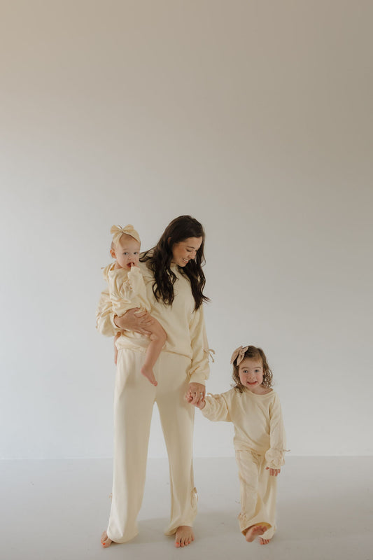 A woman in a forever french baby Women's Sweat Set | Buttercream Bows stands smiling with two children, both in matching children’s sets with bows, against a plain light background.