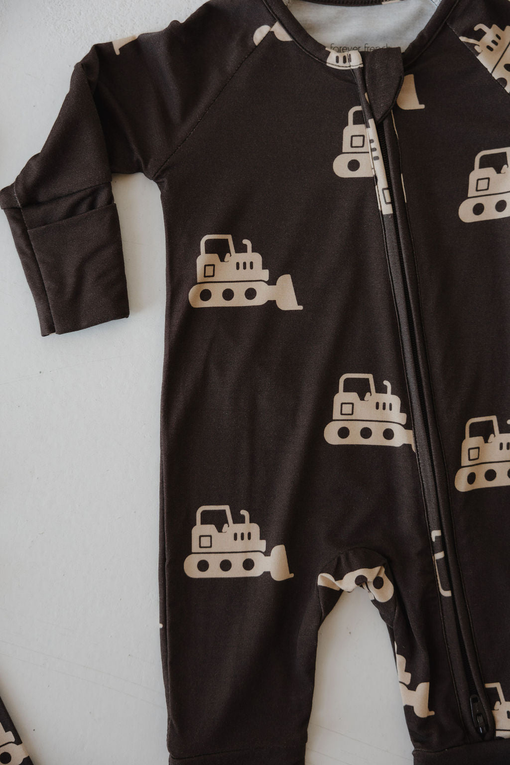 The forever french baby Bamboo Zip Pajamas | Bulldozer is a dark brown hypo-allergenic onesie with a zipper and beige bulldozers, shown flat on white—ideal cozy wear for your little one.