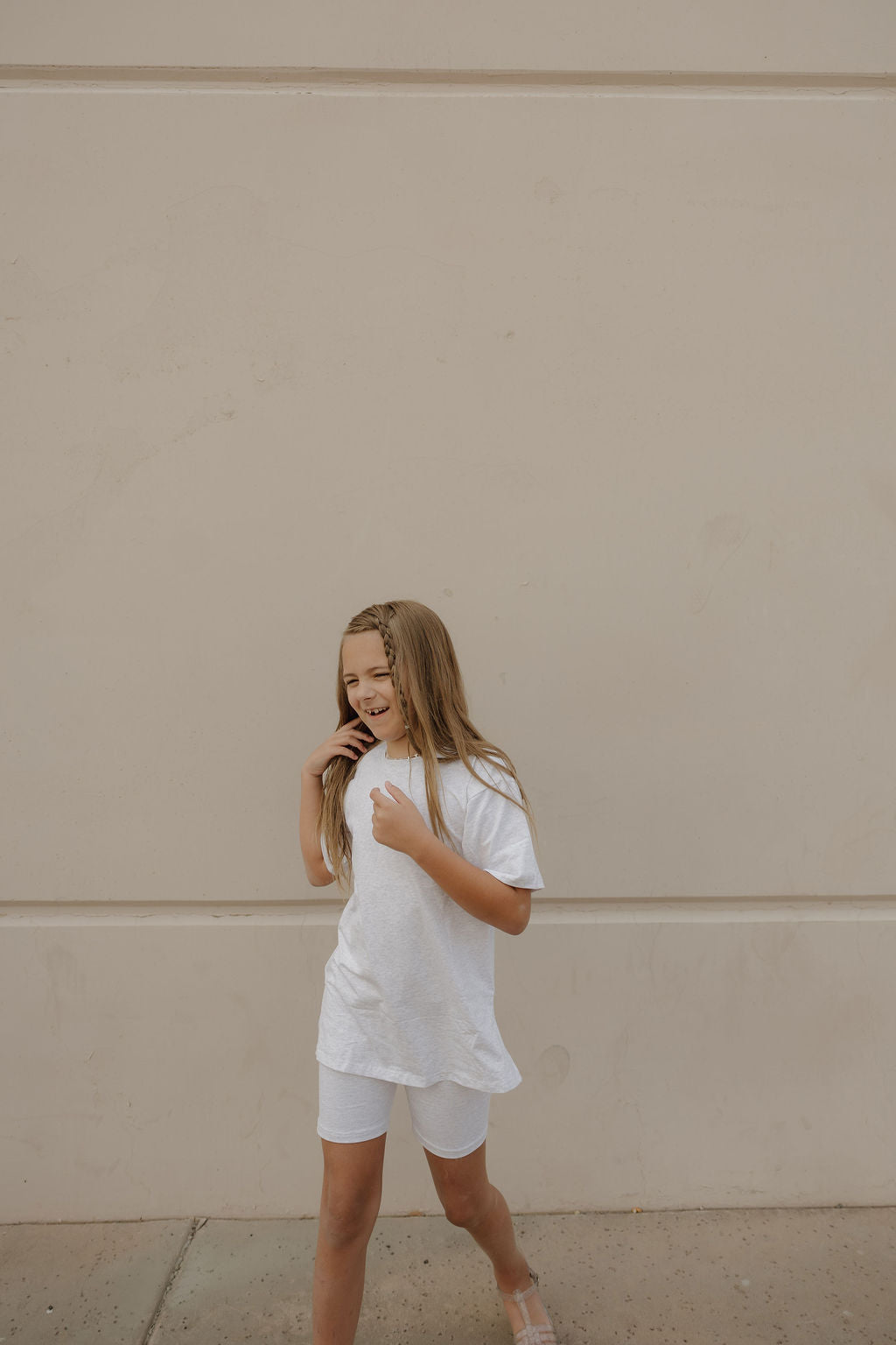 A young girl with long blonde hair wears the forever french baby Child Short Set | Heather as she smiles and looks to her left in front of a beige wall.