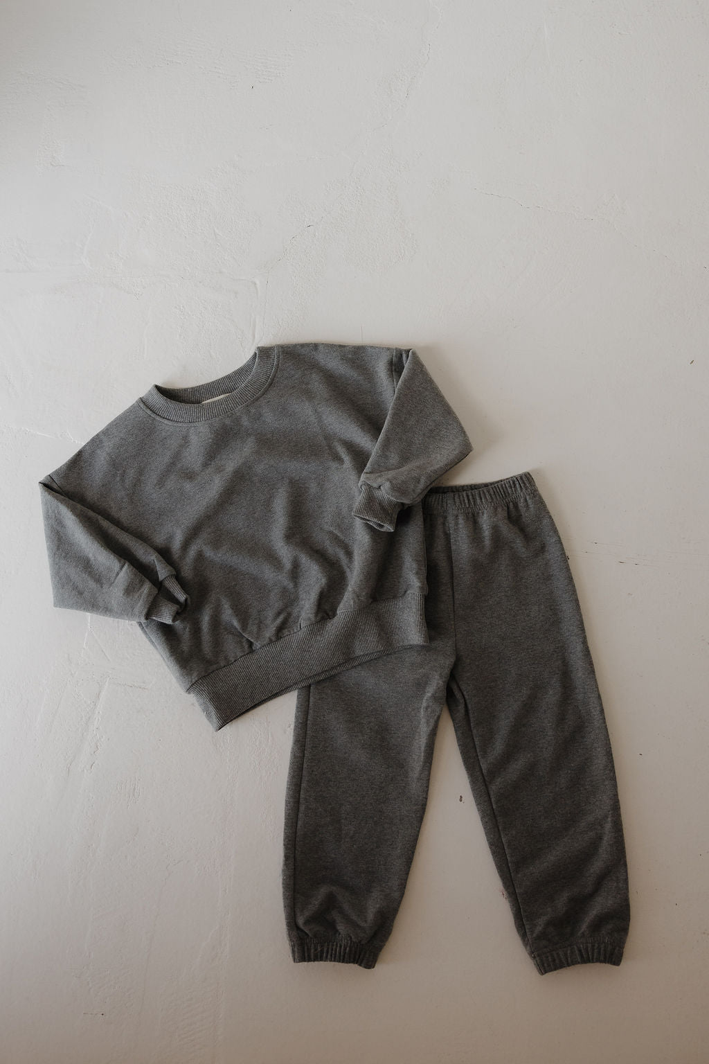 The forever french baby Child Sweat Set in Charcoal—a stylish gray long-sleeve sweatshirt and sweatpants—offers the perfect coordinated look for your little one, displayed on a light-colored surface.