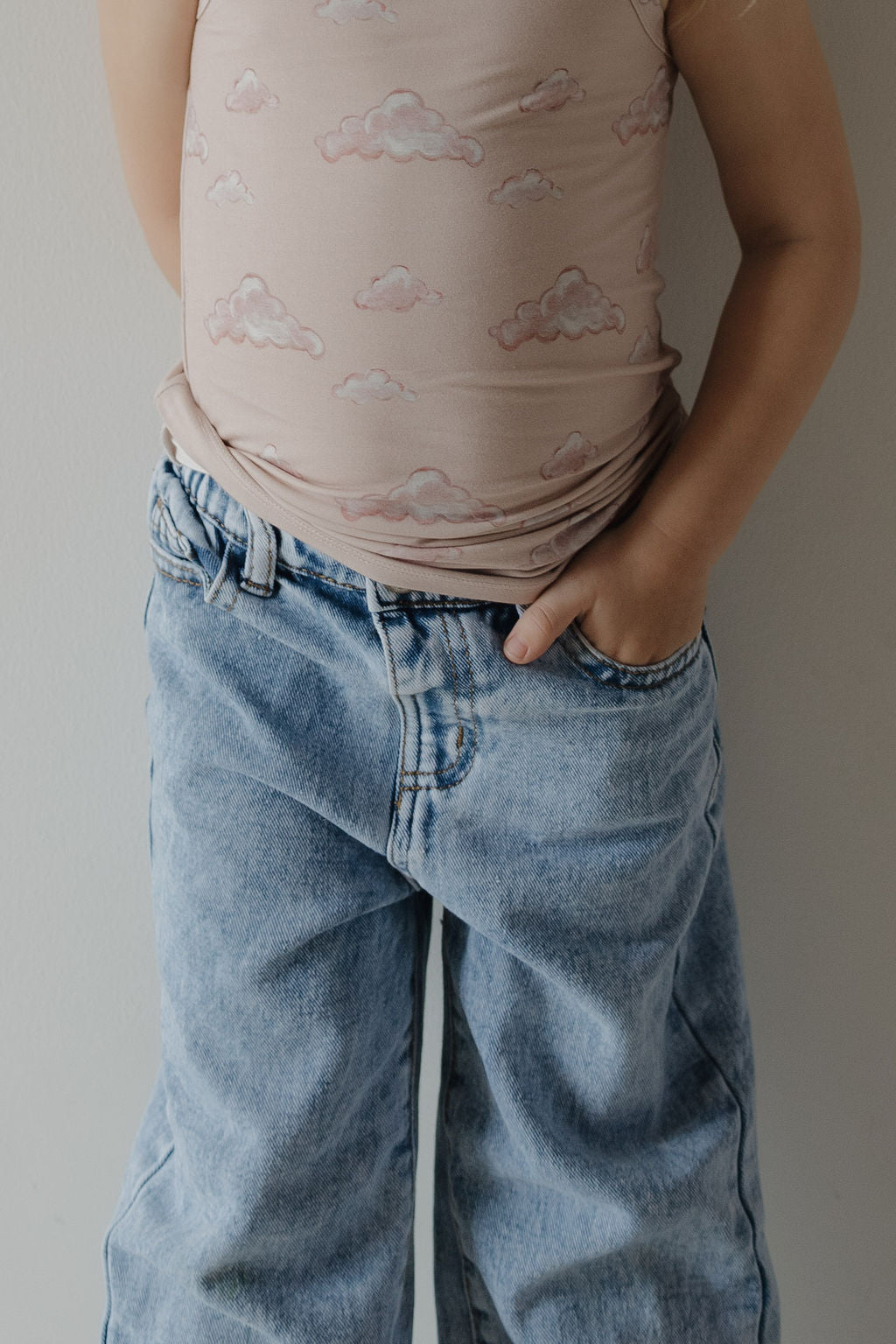 A child wears the Kendy 3 Toddler Bamboo Cami Set in Ruby, featuring a light pink, hypo-allergenic bamboo top, and stands with one hand in their pocket against a plain background.