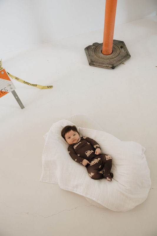 A baby in the forever french baby Sleepy Time Set | Bulldozer lies on a white blanket next to an orange construction cone and caution tape.