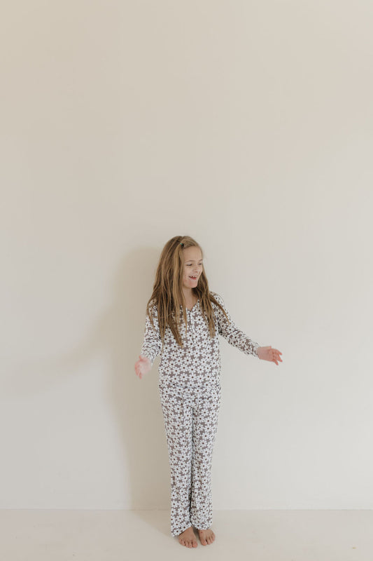 A young girl stands against a plain wall in forever french baby's Youth Flare Bamboo Pajamas | Darlin’. Her long hair flows as she smiles and looks to the side, with her hypo-allergenic, breathable bamboo floral pajamas highlighted against the minimalistic background.