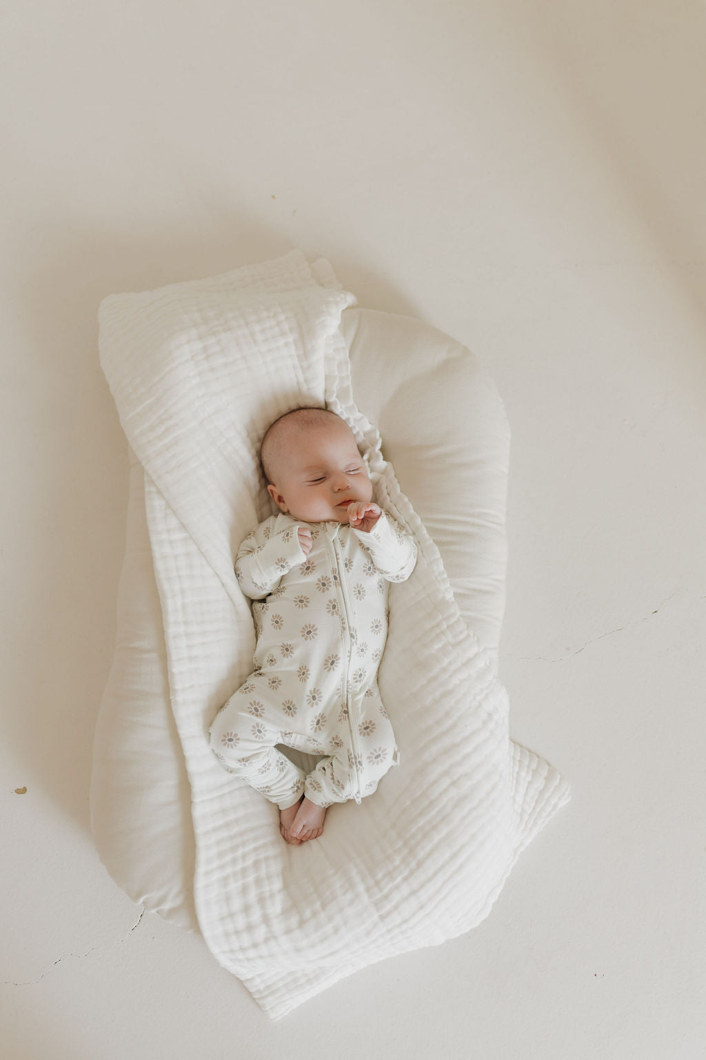 A baby in forever french baby's Bamboo Zip Pajamas | Daisy Fields peacefully sleeps on a soft, white cushion against a minimalistic, light neutral background, creating a serene and cozy atmosphere perfect for showcasing hypo-allergenic clothing.