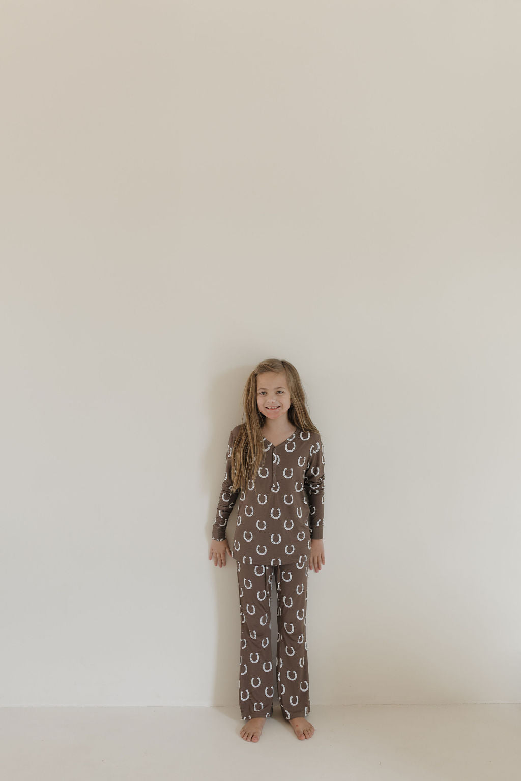 A young girl with long hair stands barefoot against a plain background, wearing Youth Flare Bamboo Pajamas | Giddy Up by forever french baby.